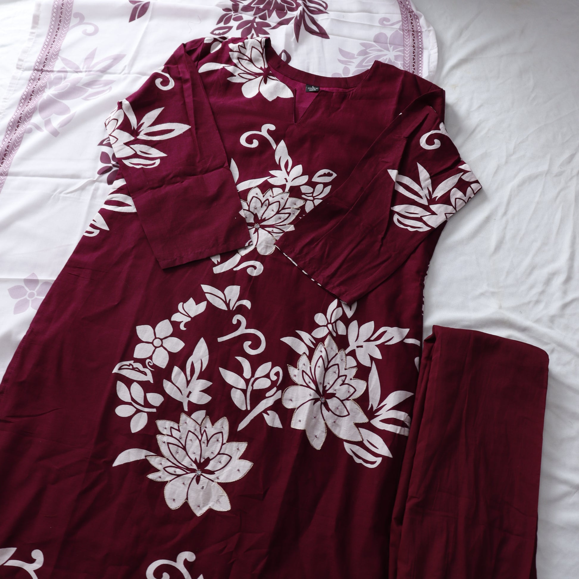 Maroon pajama set with white floral patterns on a white bedspread.